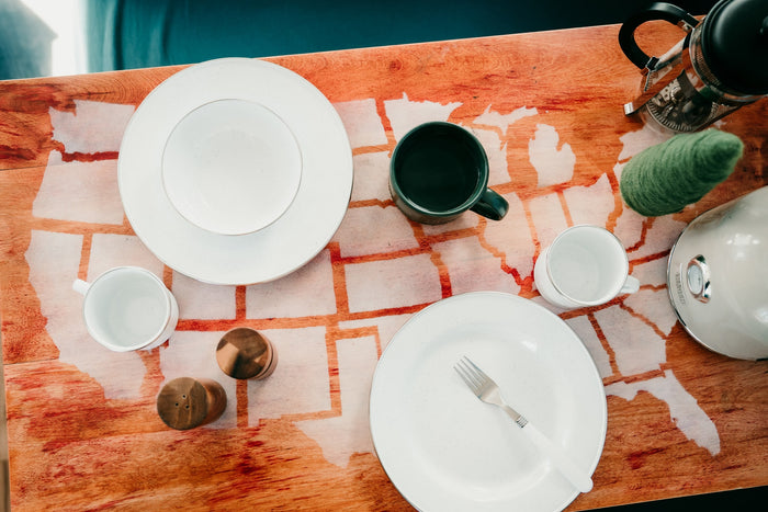 RV rental dining: white dishes, mugs, French press, and kettle on a wood table with U.S. state map outlines.