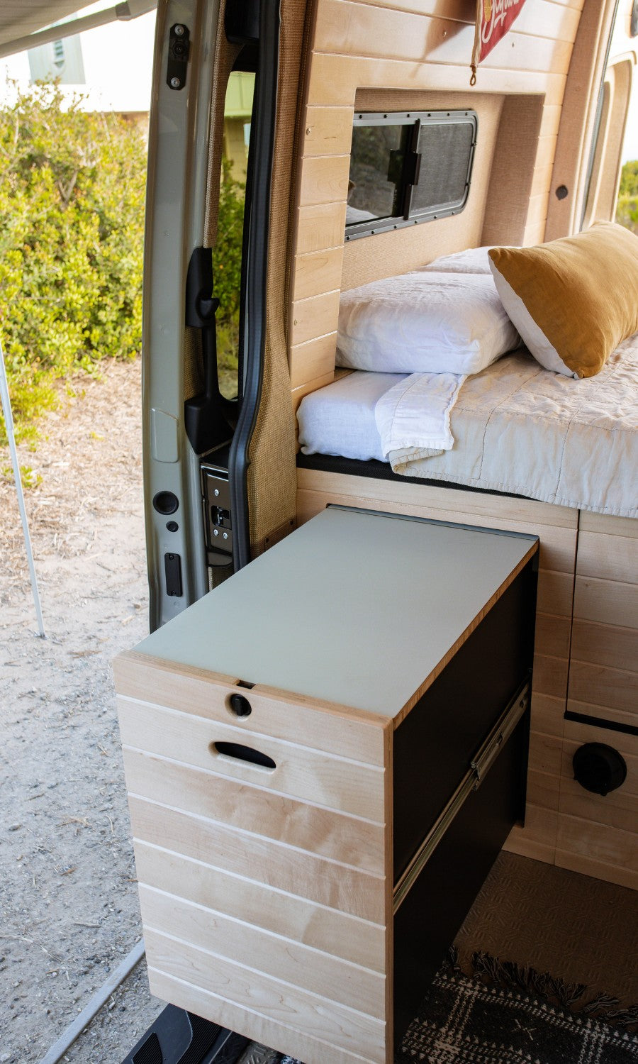 Cozy RV rental interior with a bed, wood paneling, and a pull-out storage unit, seen from the open side door.