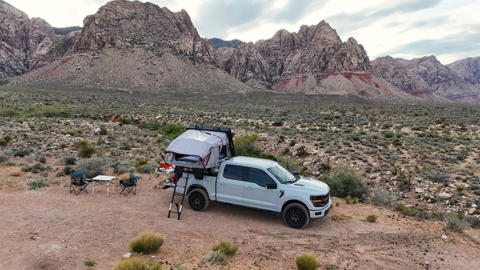 RV rental adventure! Pickup truck with rooftop tent set up for desert camping amid stunning mountains.