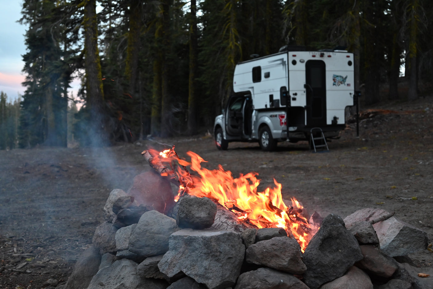 Camping under the trees with a crackling campfire and a truck camper, perfect for an RV rental trip.