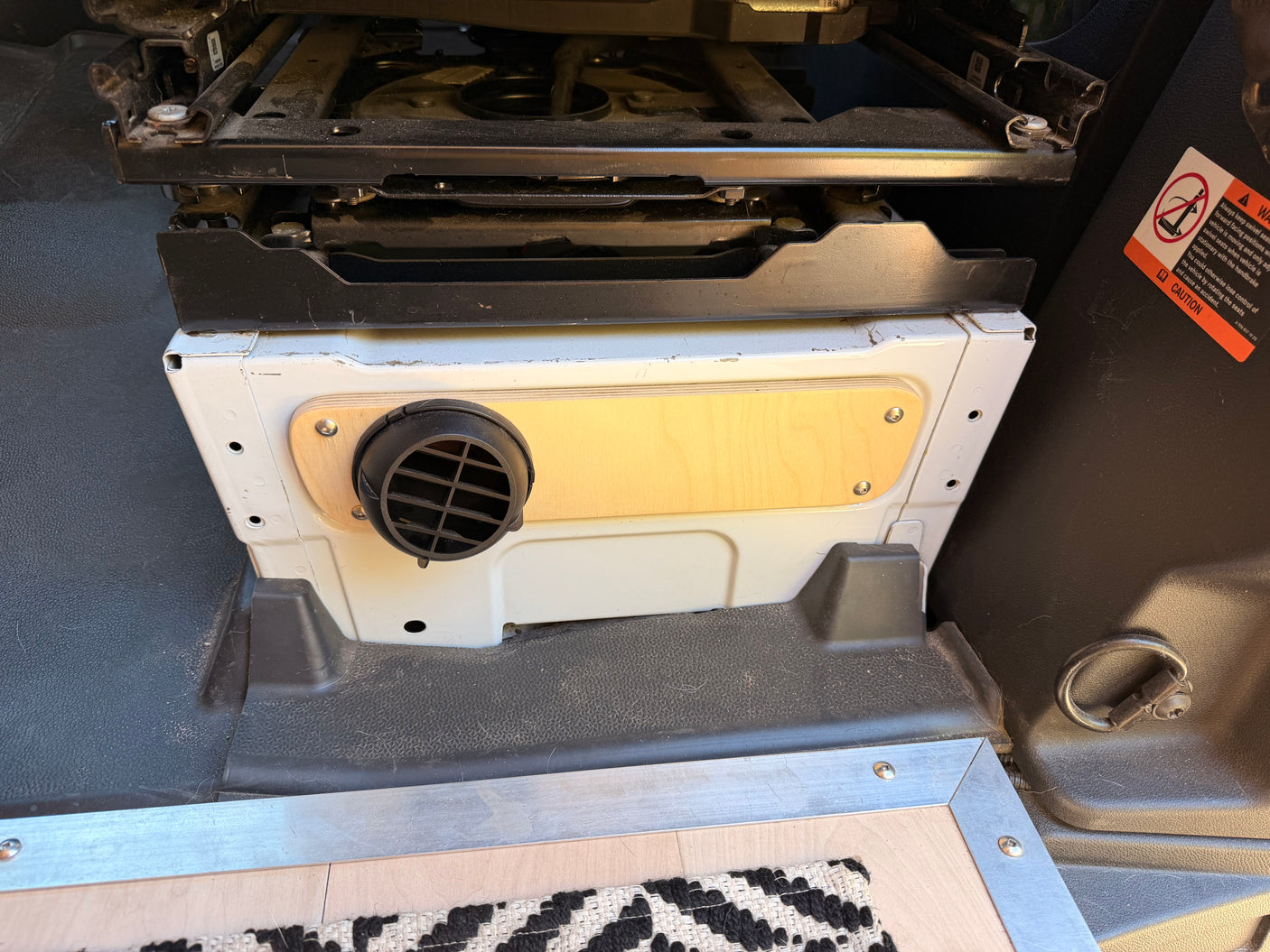 RV rental camper van interior featuring a passenger swivel seat base over a functional heater vent with wooden trim, enhancing comfort.