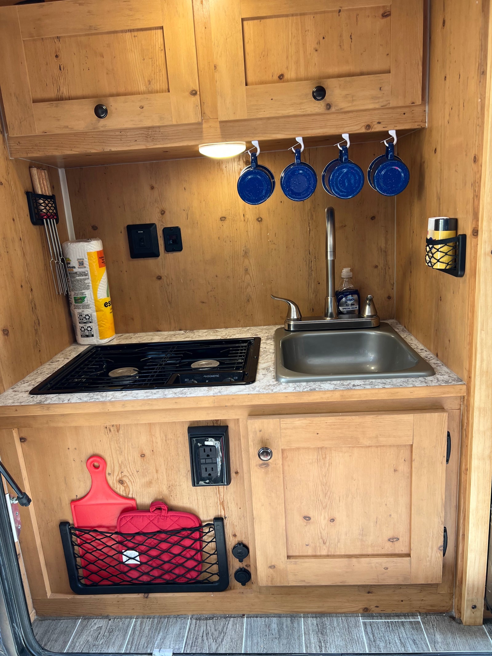 Explore this compact RV rental kitchen featuring a stove, sink, paper towels, and smart storage for mugs & utensils.