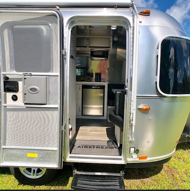 Step inside this Airstream travel trailer RV rental. Its open door reveals a compact kitchen with a fridge & microwave.