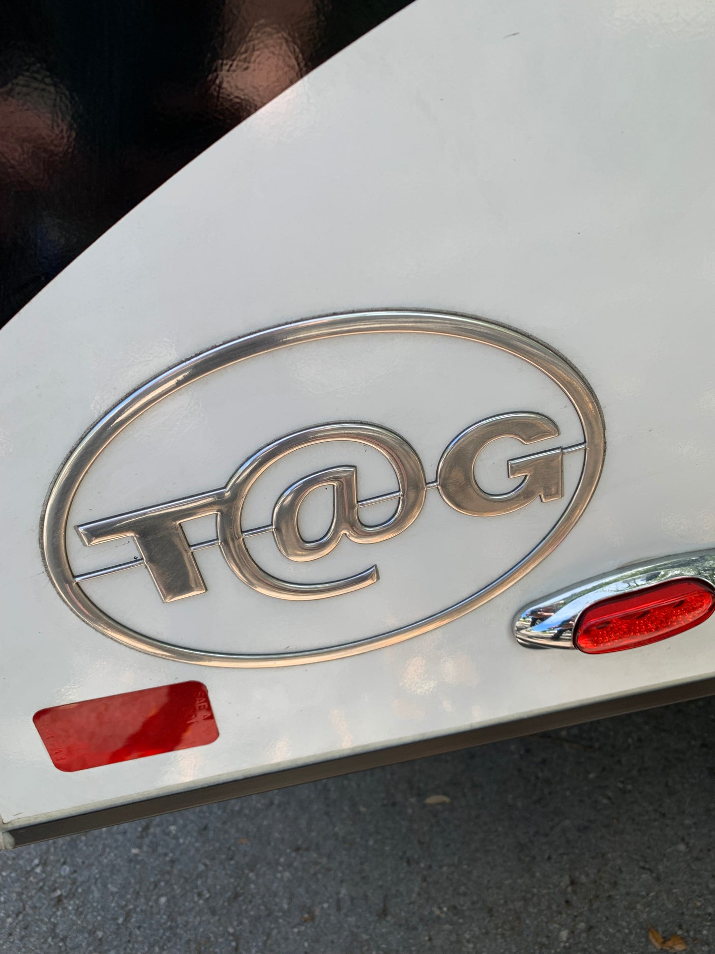 Close-up of a white and black T@G rv rental, showing its silver emblem, red reflector, and LED light.