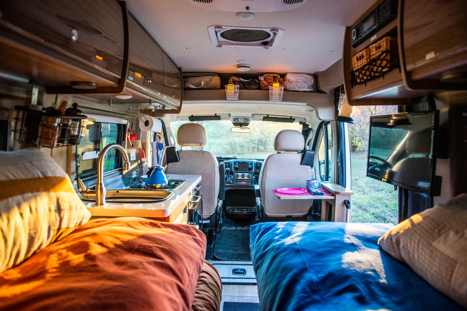 Cozy RV rental interior with kitchen, sleeping areas, and the front cabin view towards nature.