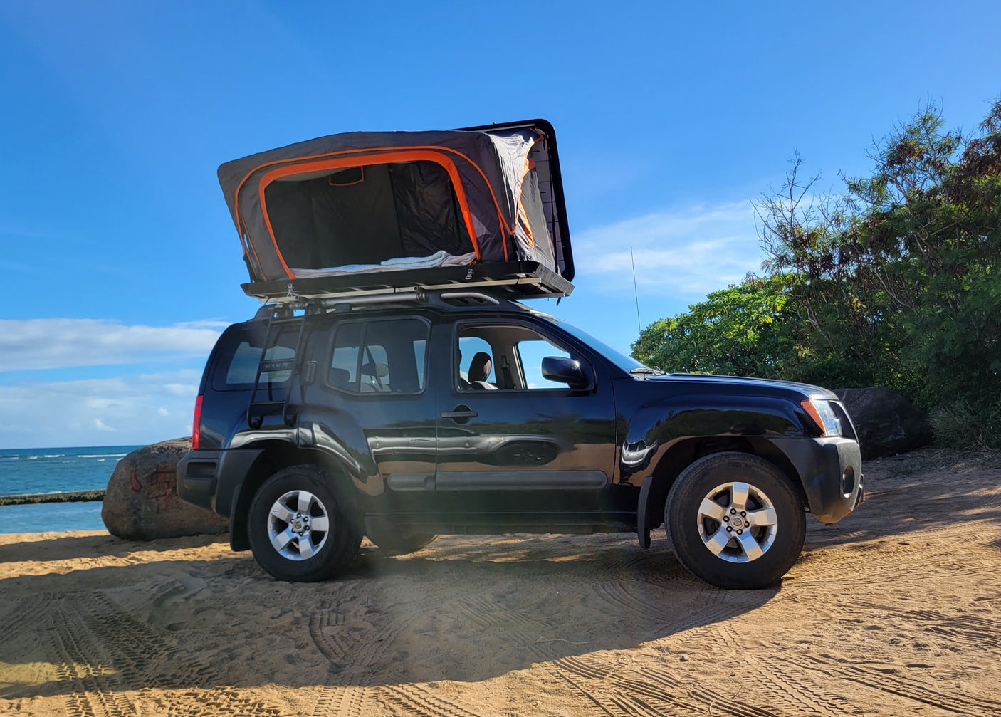 Experience beach camping with this RV rental alternative: a Nissan Xterra SUV with a deployed rooftop tent by the ocean.