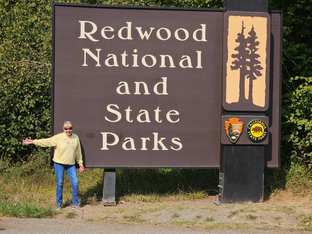 Happy traveler at Redwood National and State Parks sign, perfect for an RV rental adventure.