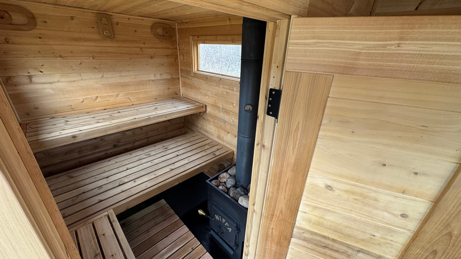 Cozy wooden sauna interior with stacked benches, a wood stove, and window. Ideal for an RV rental retreat.