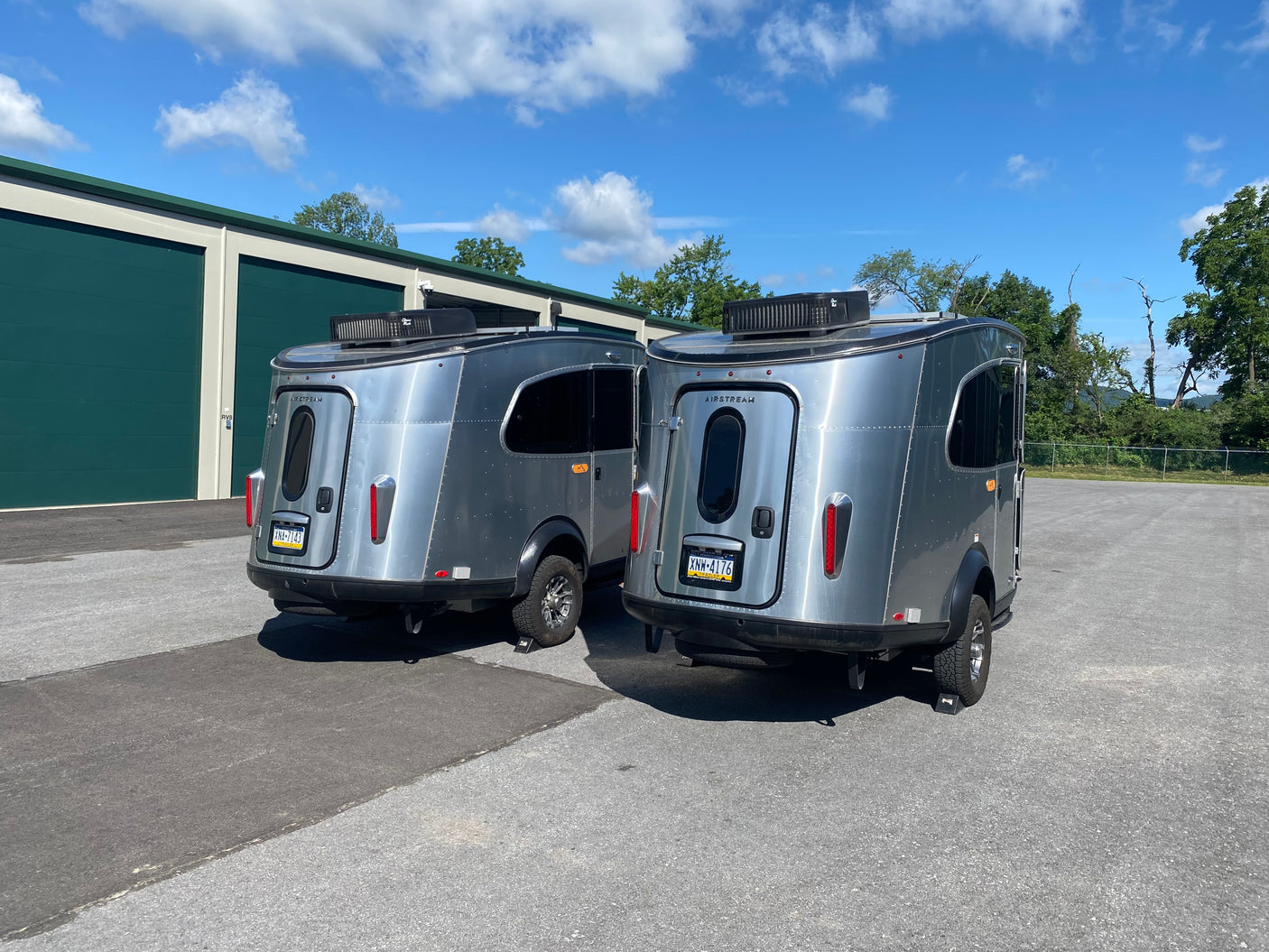 Two silver Airstream travel trailers, ideal for rv rental adventures, parked next to a green storage building on a sunny day.