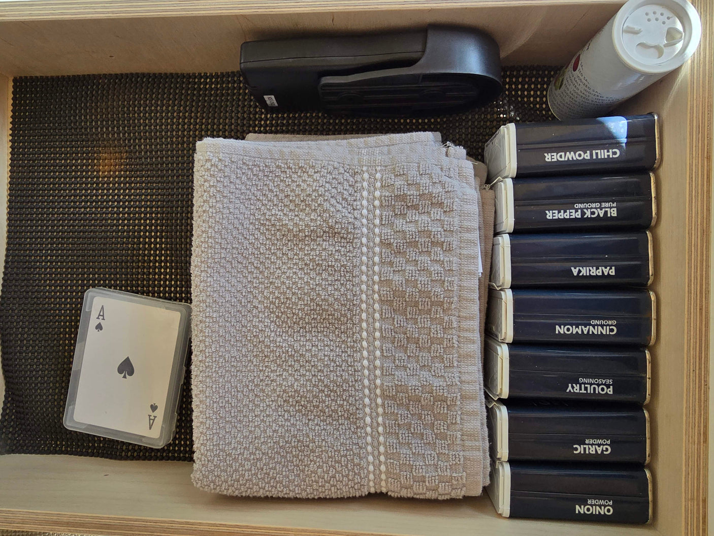 RV rental kitchen drawer with neatly stacked spices, salt, a stapler, playing cards, and a folded towel.