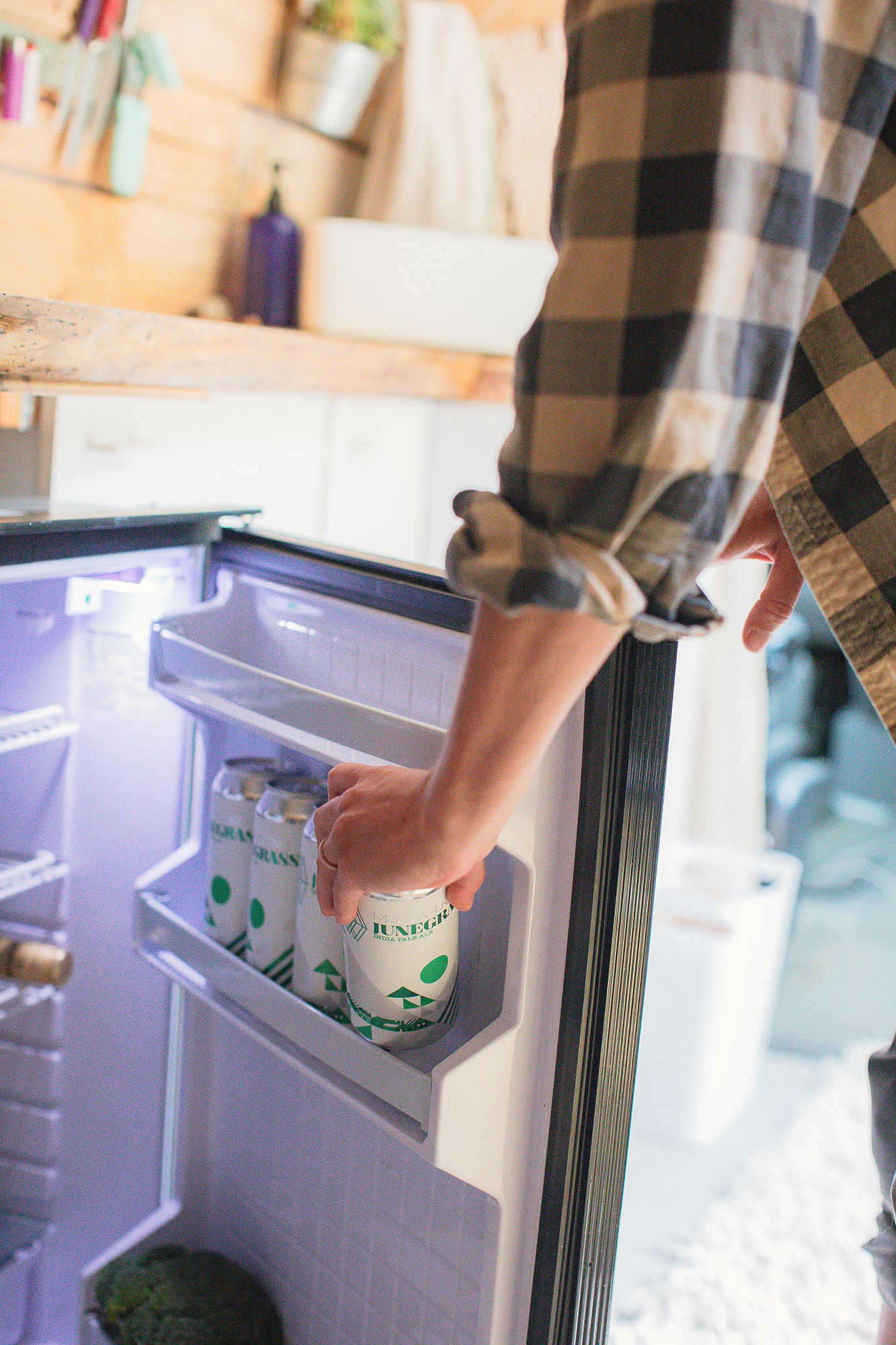 A hand reaches for a Junegrass IPA in a compact fridge, perfect for your next RV rental road trip.