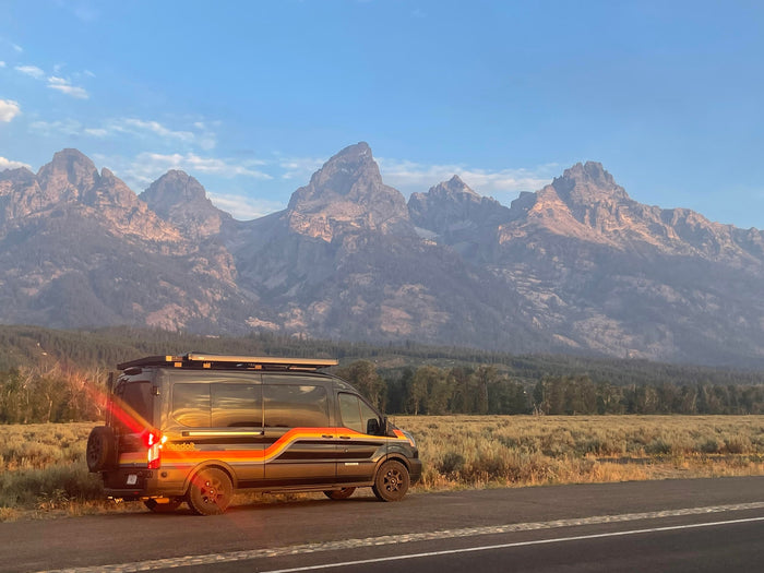 Experience an RV rental in the Tetons! A stylish Vandoit camper van awaits by the road, framed by majestic mountains.