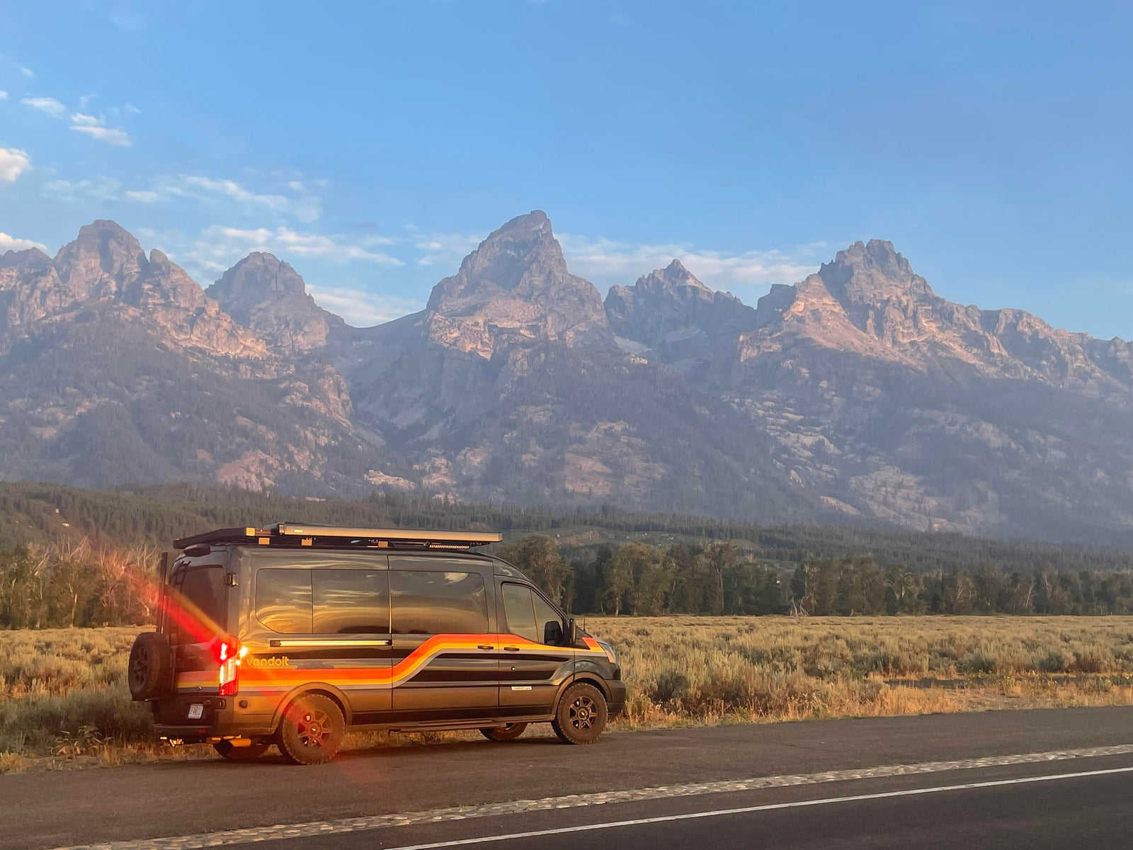 Experience an RV rental in the Tetons! A stylish Vandoit camper van awaits by the road, framed by majestic mountains.