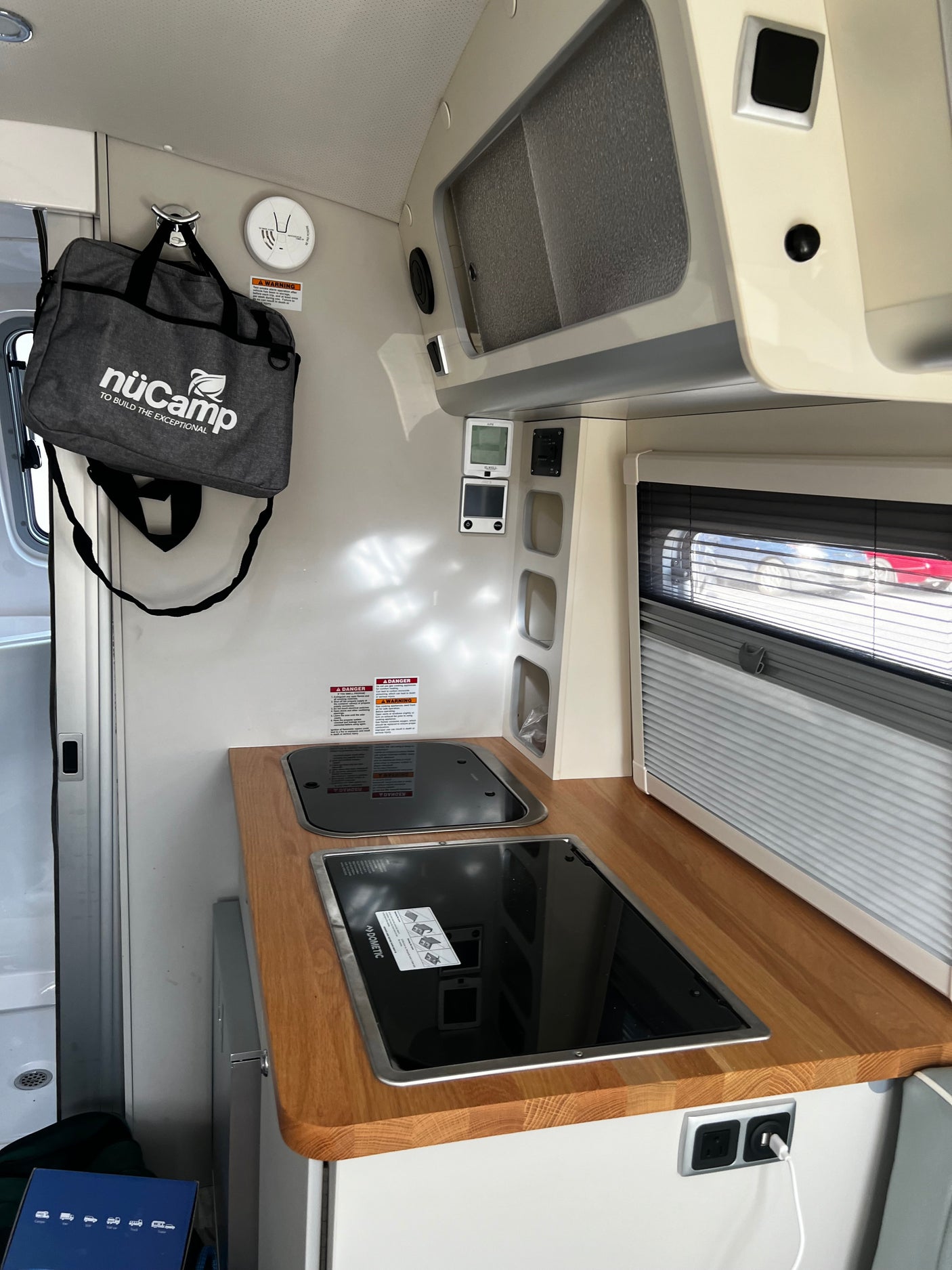Modern RV rental interior showcasing a compact kitchenette with sink, cooktop, smart controls, and overhead storage.