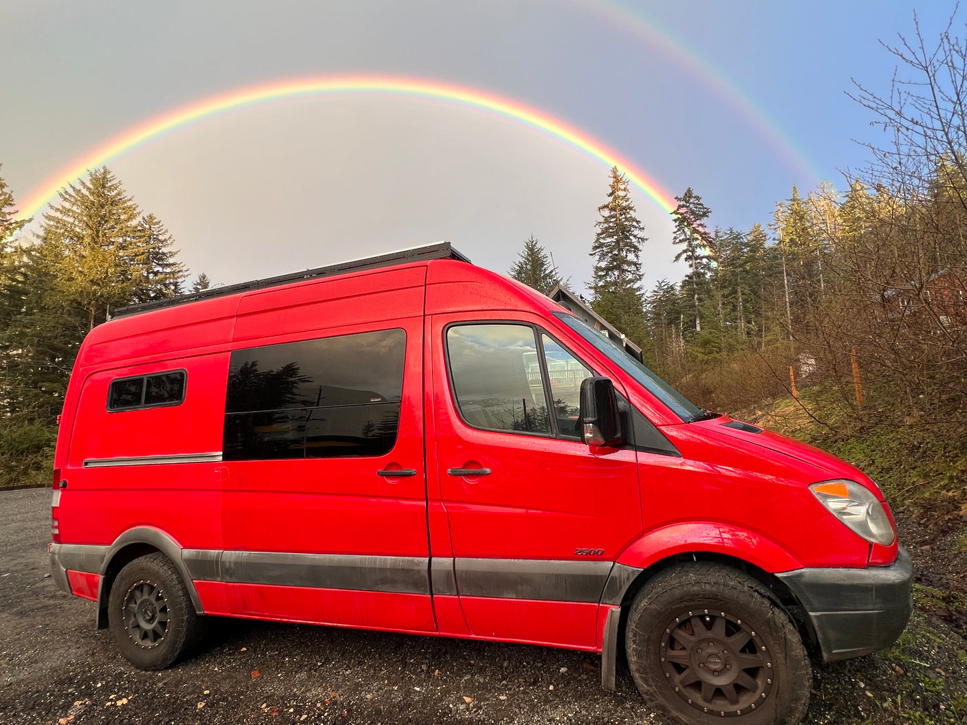 Red RV rental van parked outdoors, beneath a stunning double rainbow. Ready for adventure!