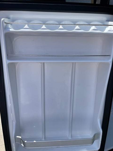 Empty, clean mini-fridge interior in an RV rental. Features a beverage caddy & molded shelf slots for organized storage.