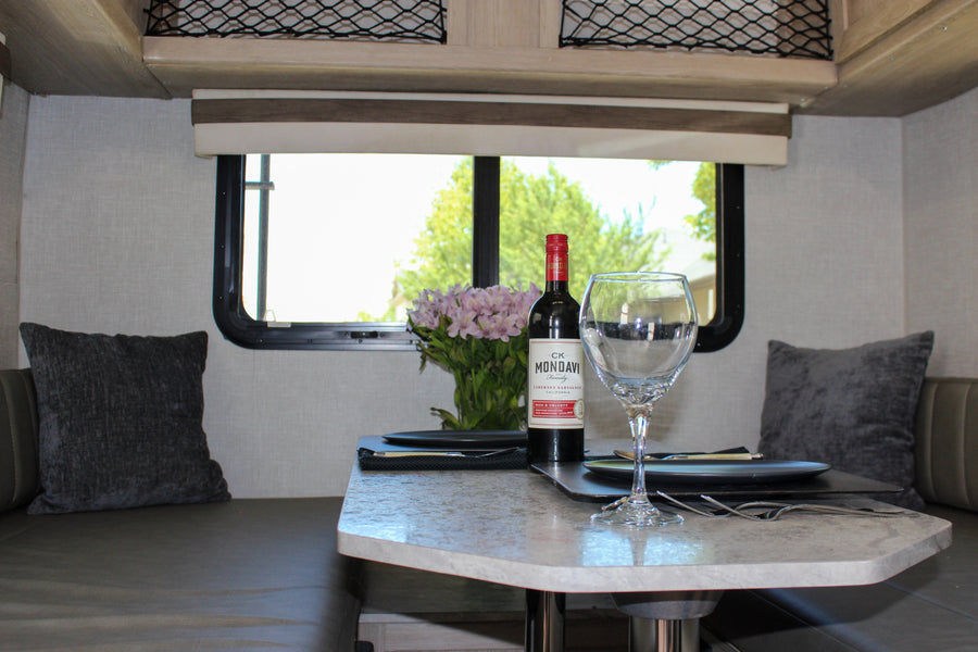 Relax in this RV rental's inviting dinette, featuring wine, fresh flowers, and comfortable seating with pillows.
