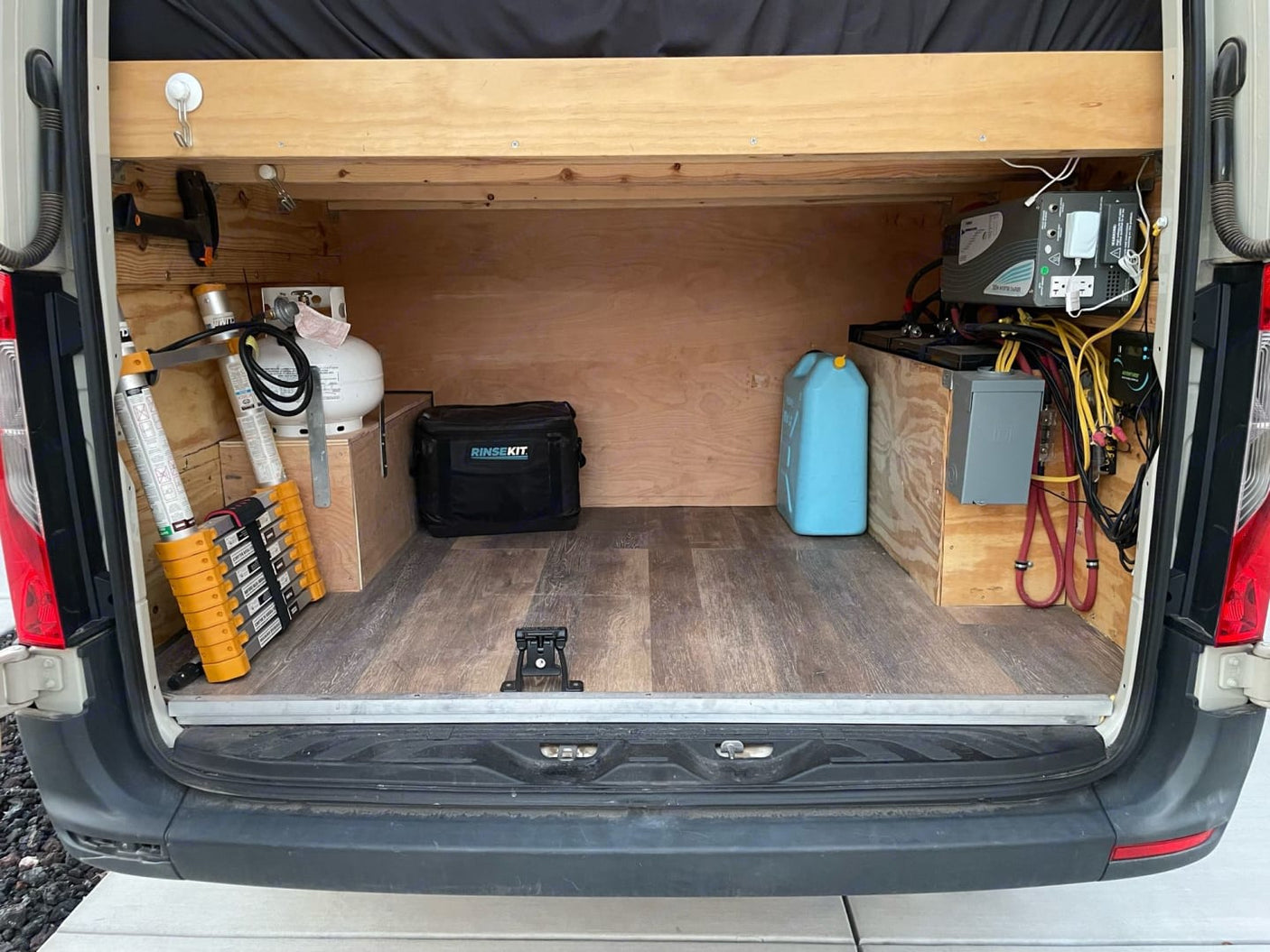 Explore the organized cargo space of an RV rental: propane tank, portable shower, telescoping ladder, battery power system, and water storage.