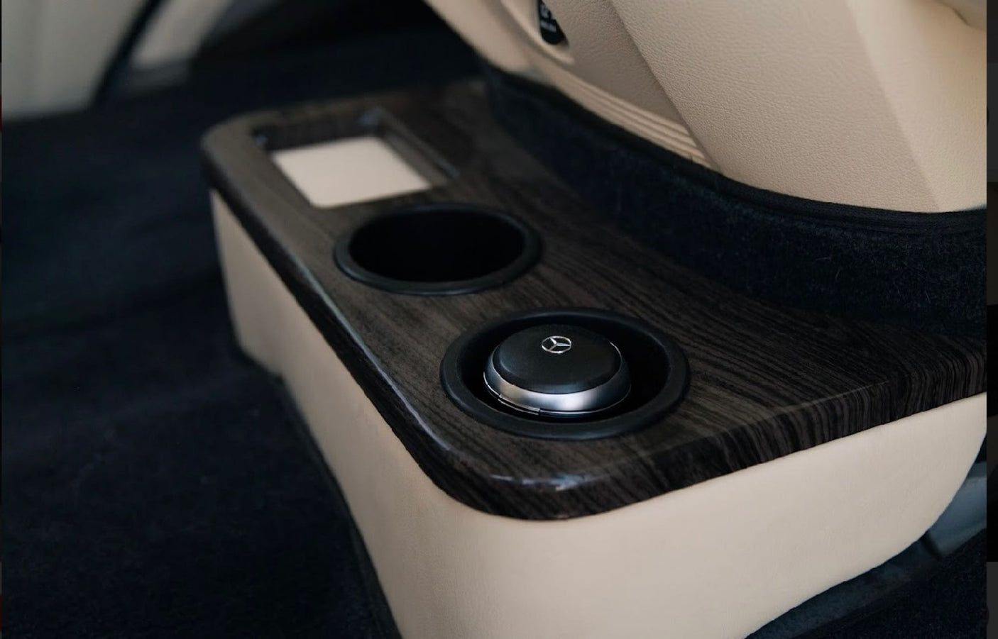 RV rental interior: Dark wood grain console with a cup holder and a Mercedes control knob, plush beige upholstery.