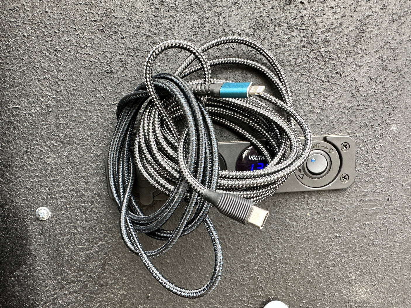 Braided USB-C & Lightning cable atop an RV rental's power monitor showing 12.7V. Essential for your journey.