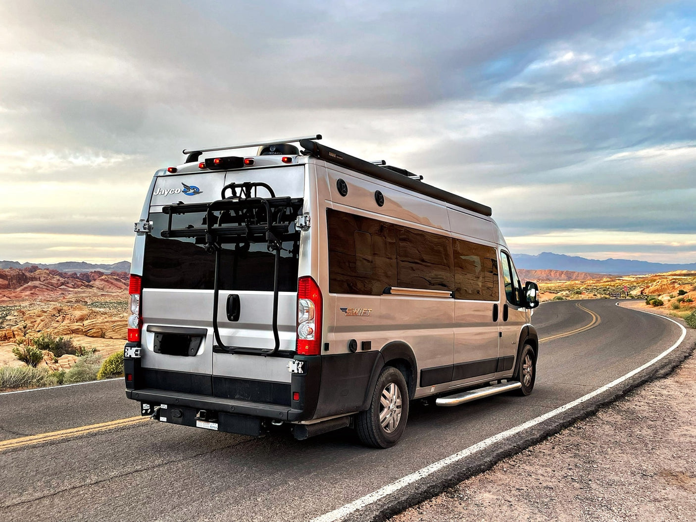 This silver rv rental camper van on a scenic desert road, ideal for your next travel adventure. See the Jayco logo!