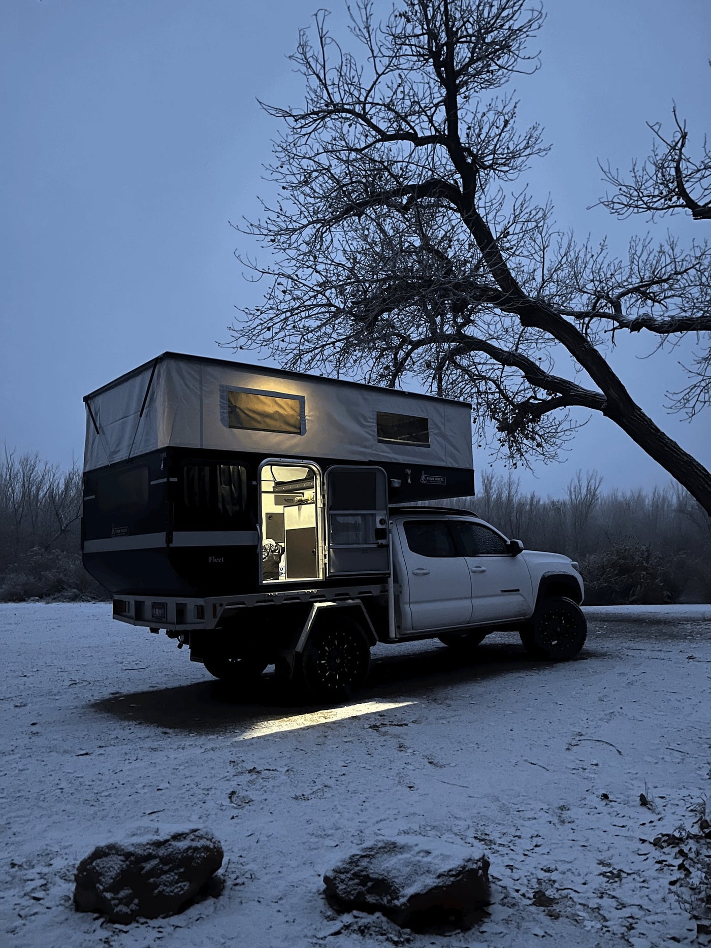 is ideal for an RV rental adventure.|This white pickup with a spacious black and white pop-up truck camper is ready for your next rv rental adventure.|Cozy RV rental: A white pickup truck with an illuminated pop-top camper in a snowy landscape with frosty bare trees.||Spacious and modern RV rental interior featuring a full kitchen — photo 5