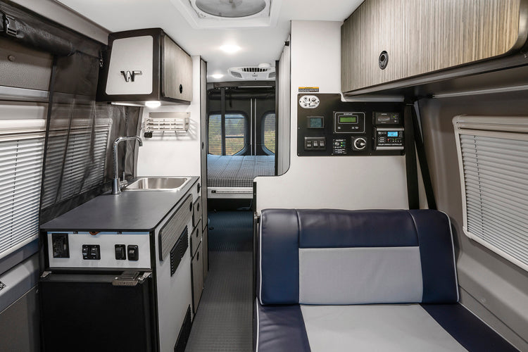 Bright rv rental interior with kitchen sink, fridge, control panel, and rear bed. Modern camper van layout.