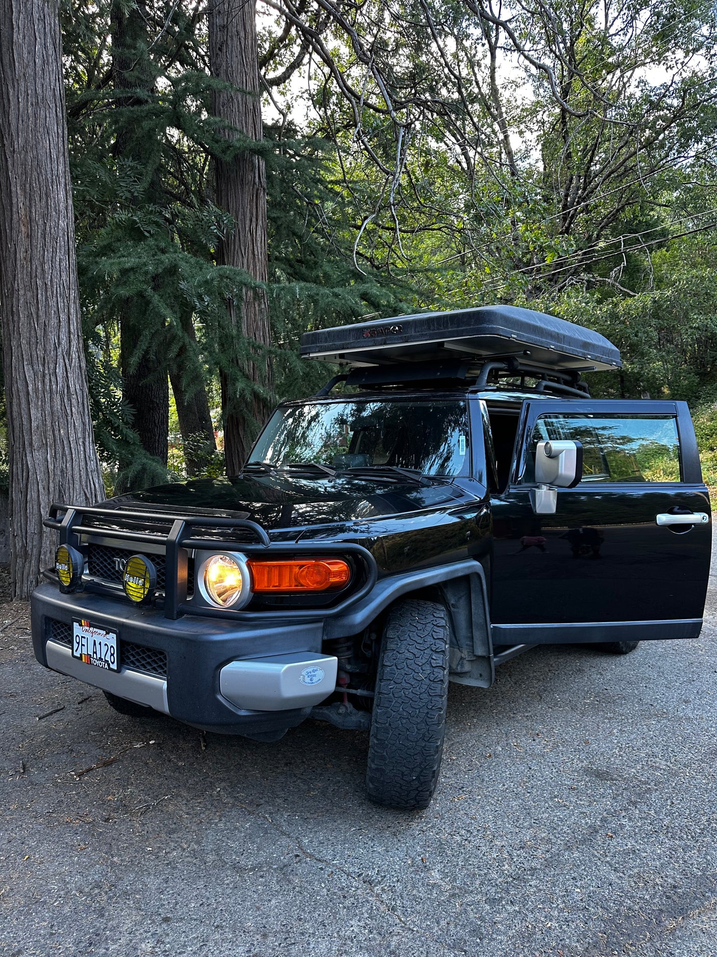 Black Toyota FJ Cruiser with a rooftop tent, parked among trees. Great rv rental for overlanding.
