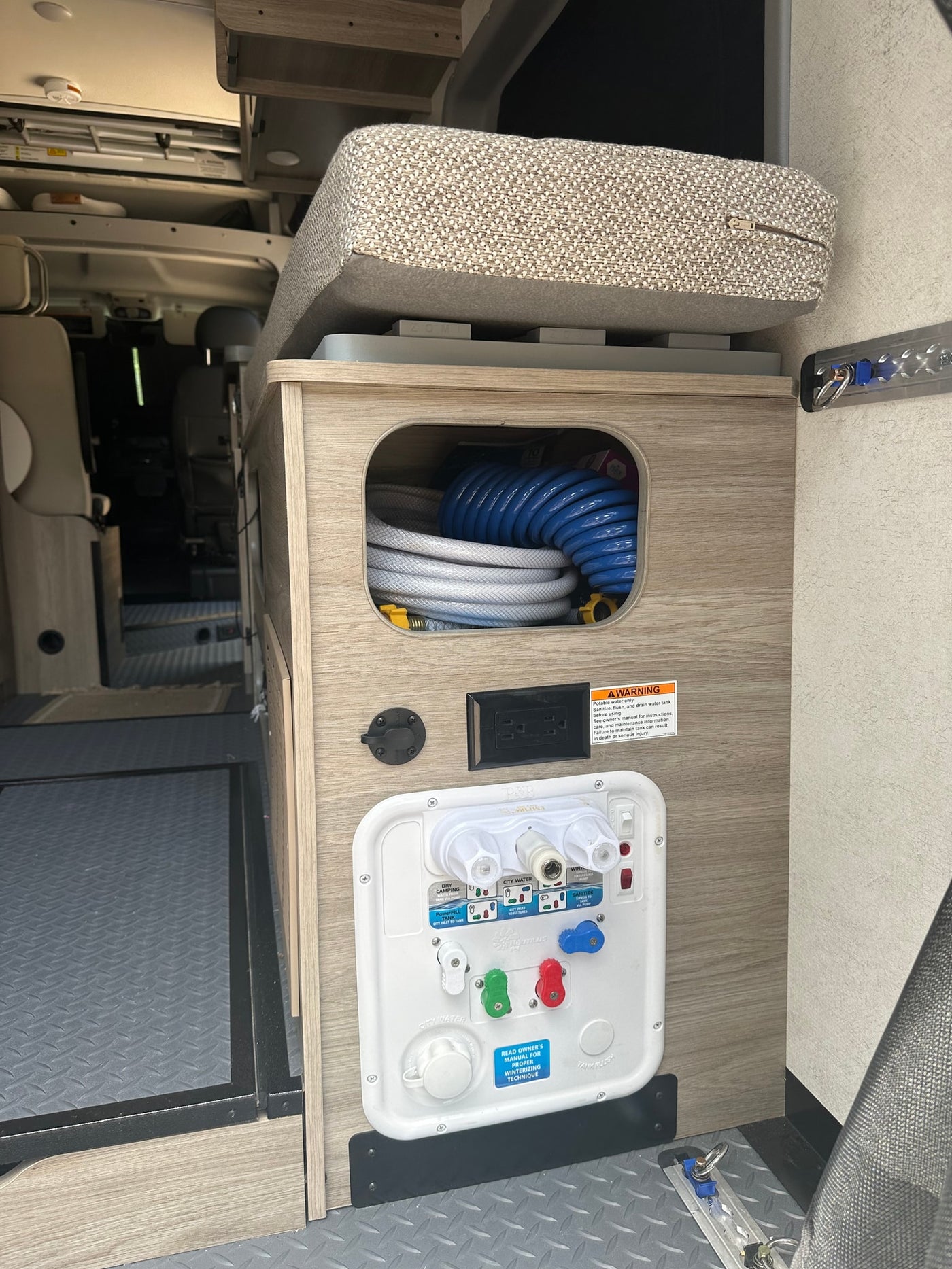 RV rental utility panel for water management, with hoses stored in the cubby inside a camper van. — photo 16