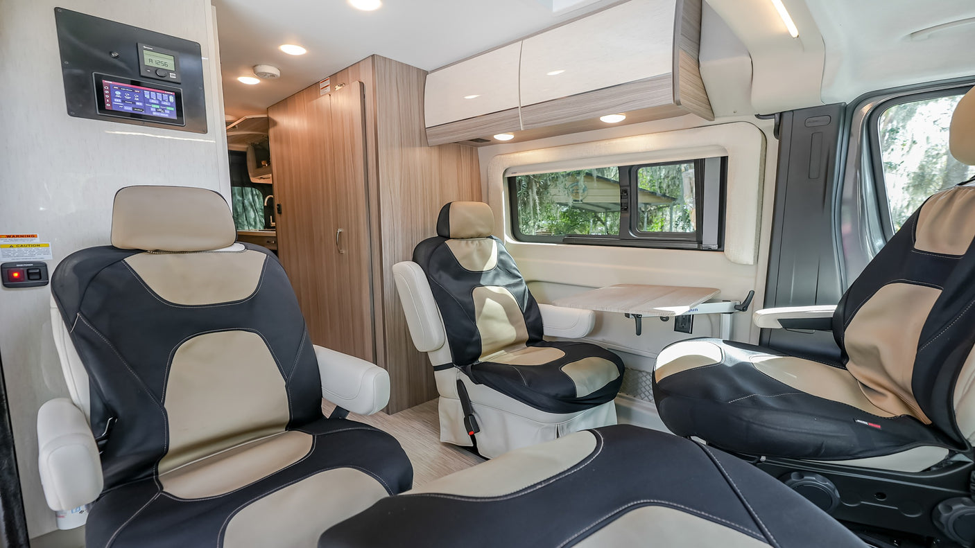 RV rental interior: Comfortable black and tan seating, control panel, fold-out table, and cabinet storage in a modern camper van.