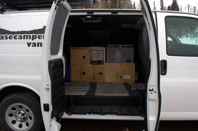 Open doors of an rv rental camper van reveal a practical custom interior with wood storage, fridge, and heater.