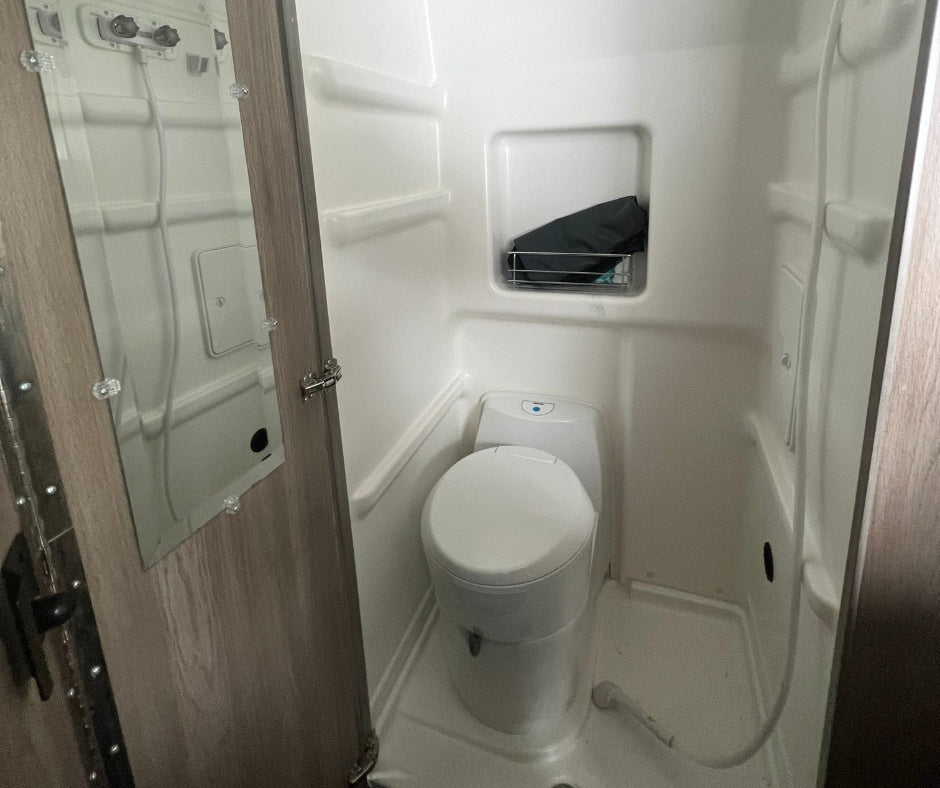 Inside an RV rental, this compact wet bath features a toilet, shower, and a mirror on the door.