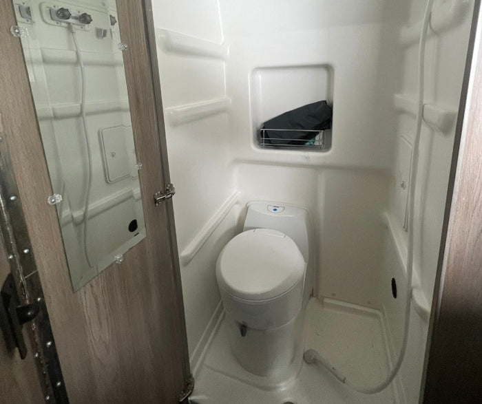 Inside an RV rental, this compact wet bath features a toilet, shower, and a mirror on the door.