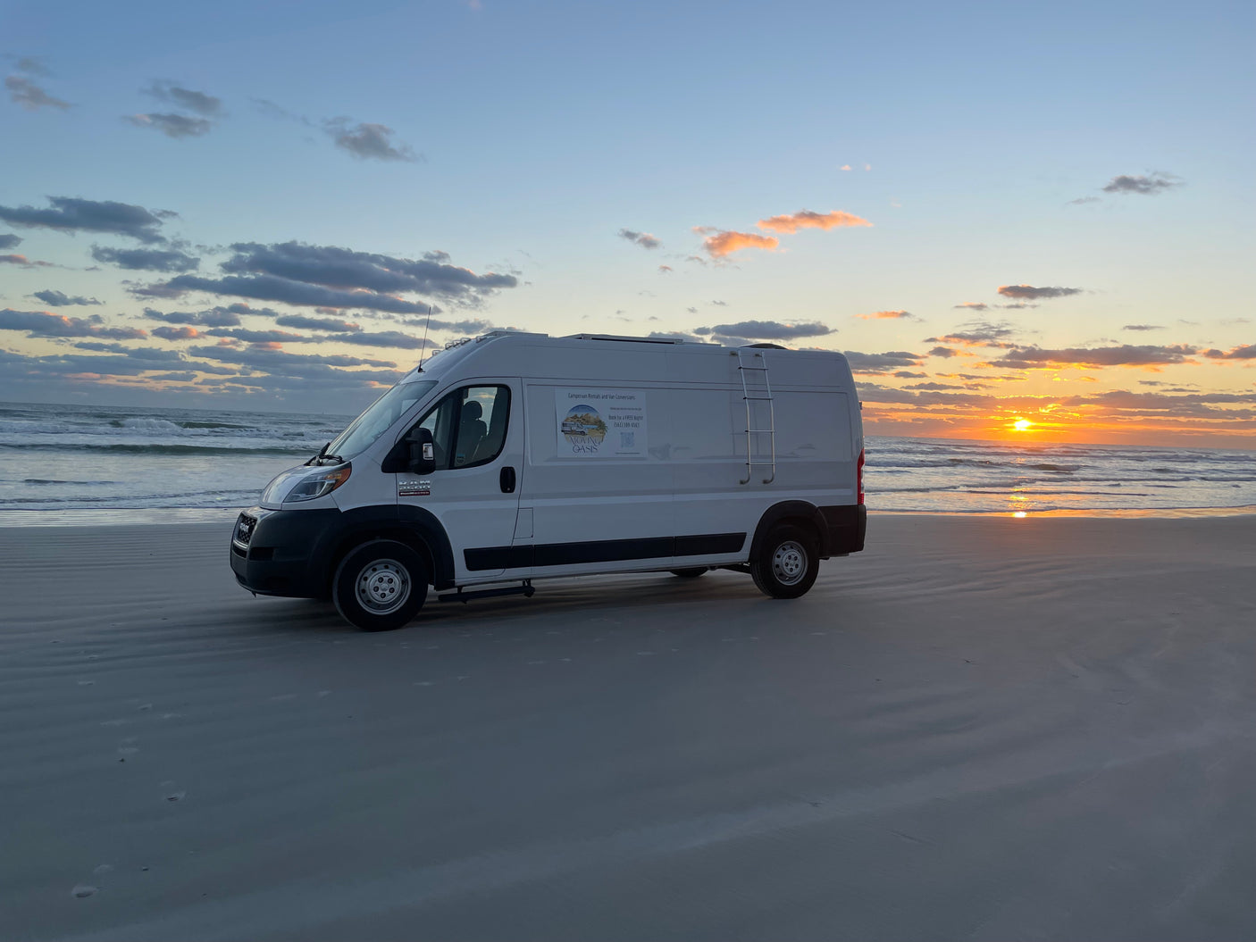 An RV rental van by Moving Oasis sits on a sandy beach at sunset, offering campervan rentals for travel adventures.