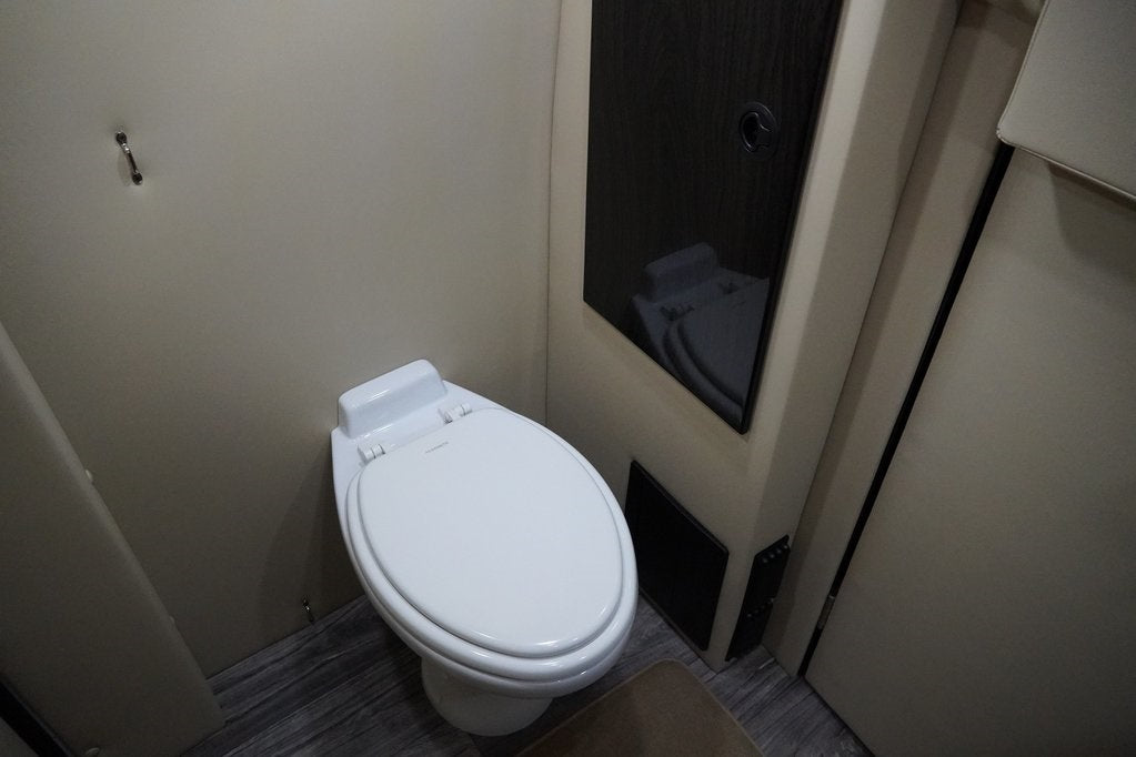 RV rental's compact bathroom features a Dometic toilet on wood flooring, with a reflective dark cabinet and beige walls.