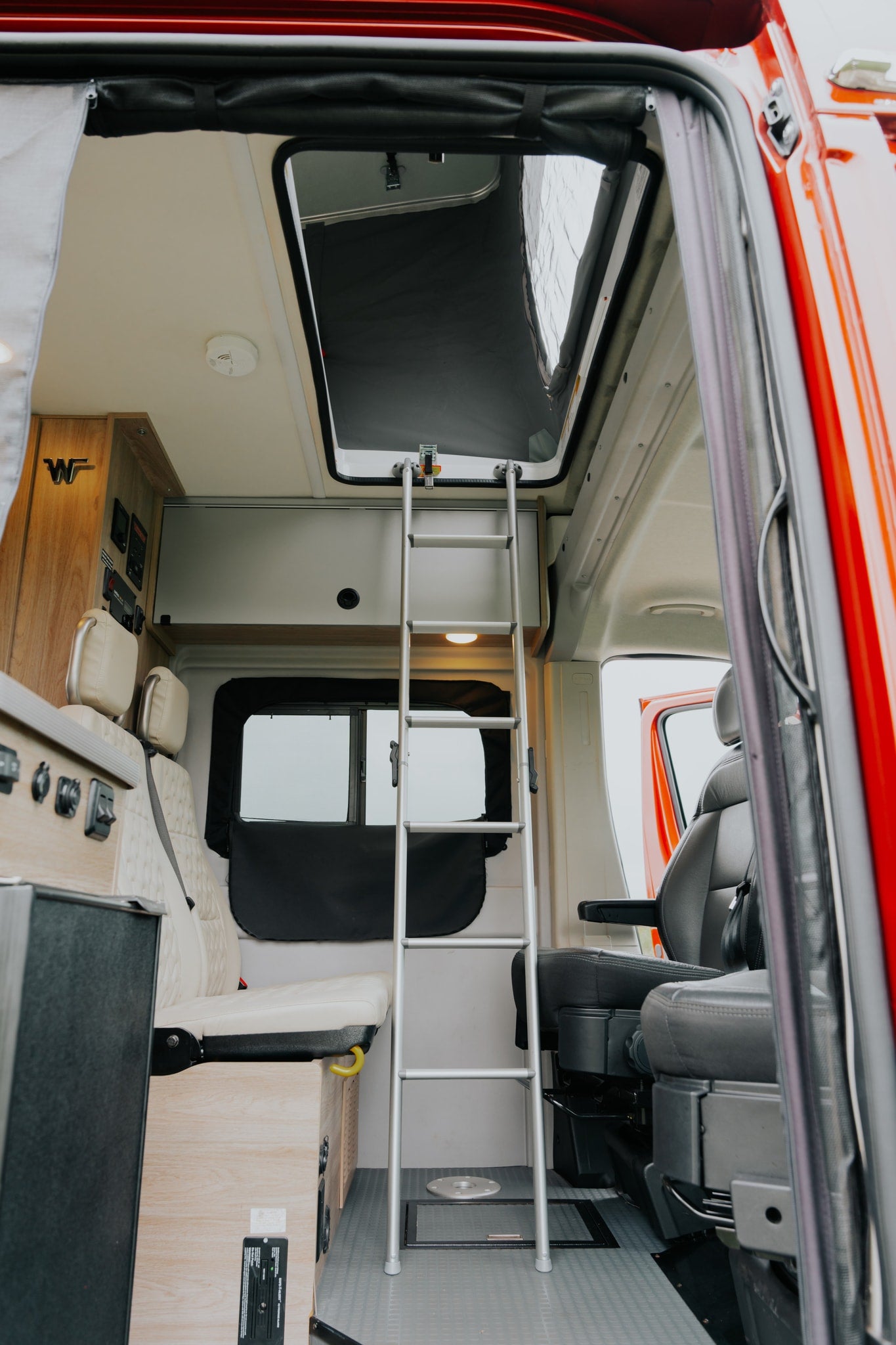 Inside an RV rental: a ladder to a pop-top bed, plush seating, and wooden cabinetry with control panels.