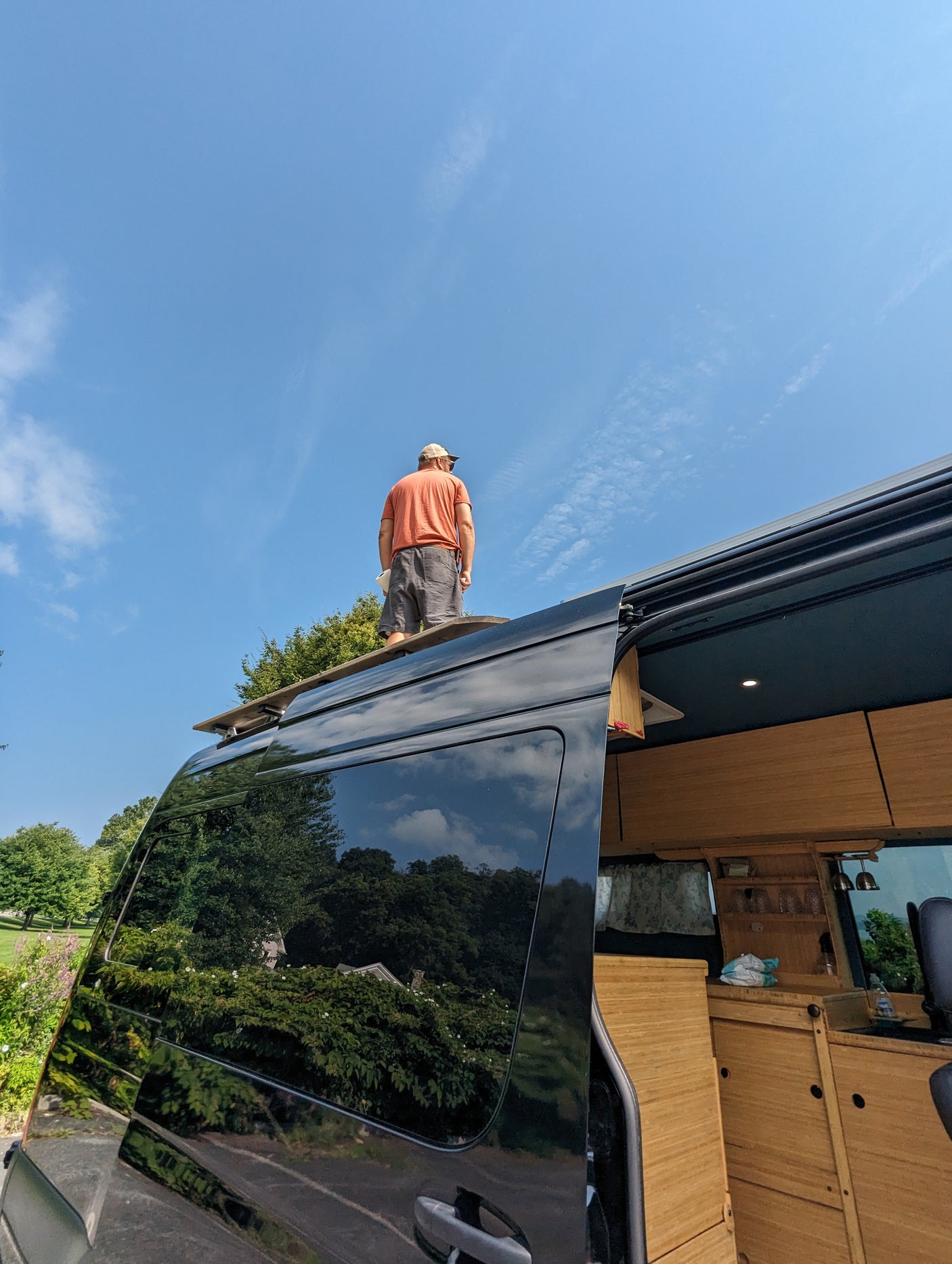 Man on an RV rental roof, admiring the view from his customized camper van. Ideal for adventure travel.