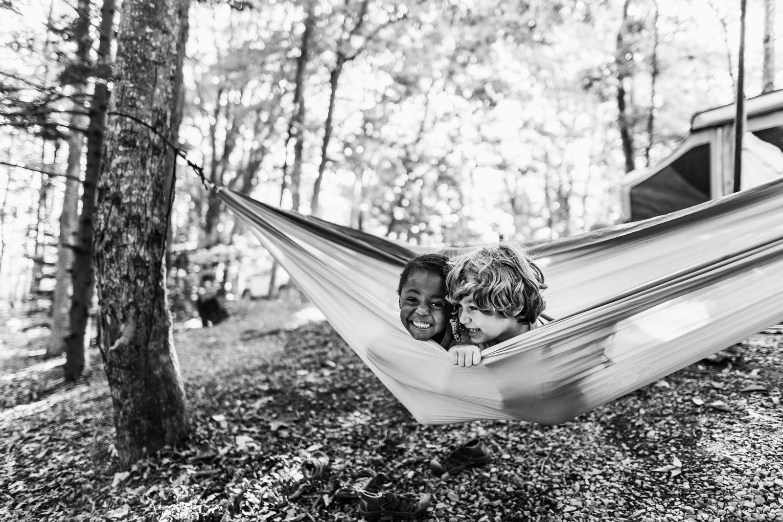 Two happy kids enjoy a hammock in the forest, near their RV rental. Great for family camping and outdoor fun.