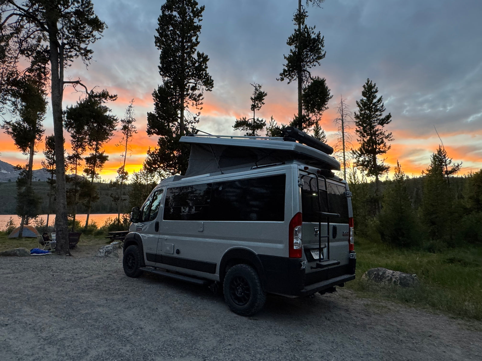 A grey RV rental camper van at a lakeside campsite, under a vibrant sunset. Ideal for camping trips.