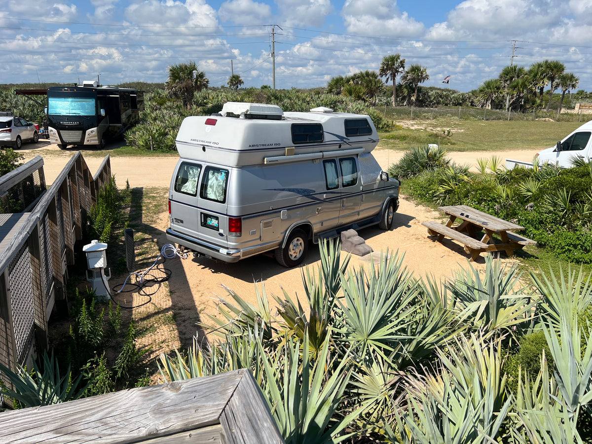RV rental: Airstream 190 camper van at a sandy Florida campsite by the beach, surrounded by palm trees and a picnic table. — photo 8