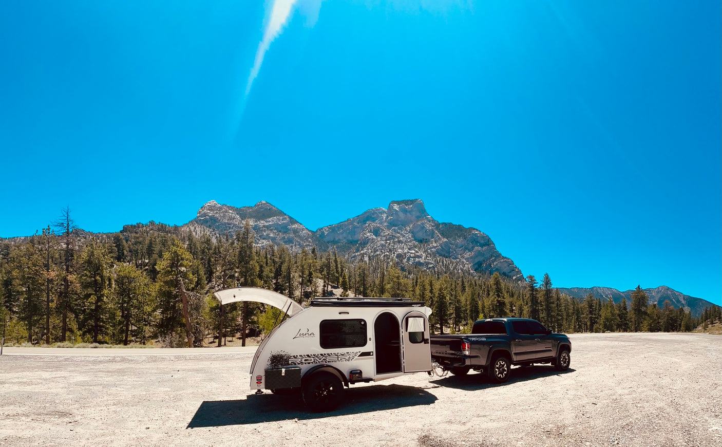 Teardrop Luna Rover RV rental & Toyota Tacoma truck in a scenic mountain setting with open doors.