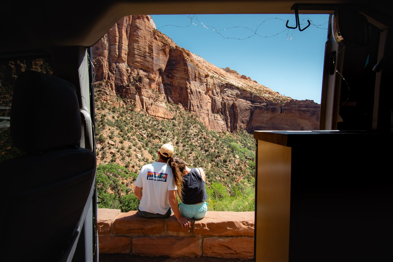 An RV rental provides the perfect mobile base for adventure! A couple sits on a scenic overlook, gazing at towering red rock mountains.