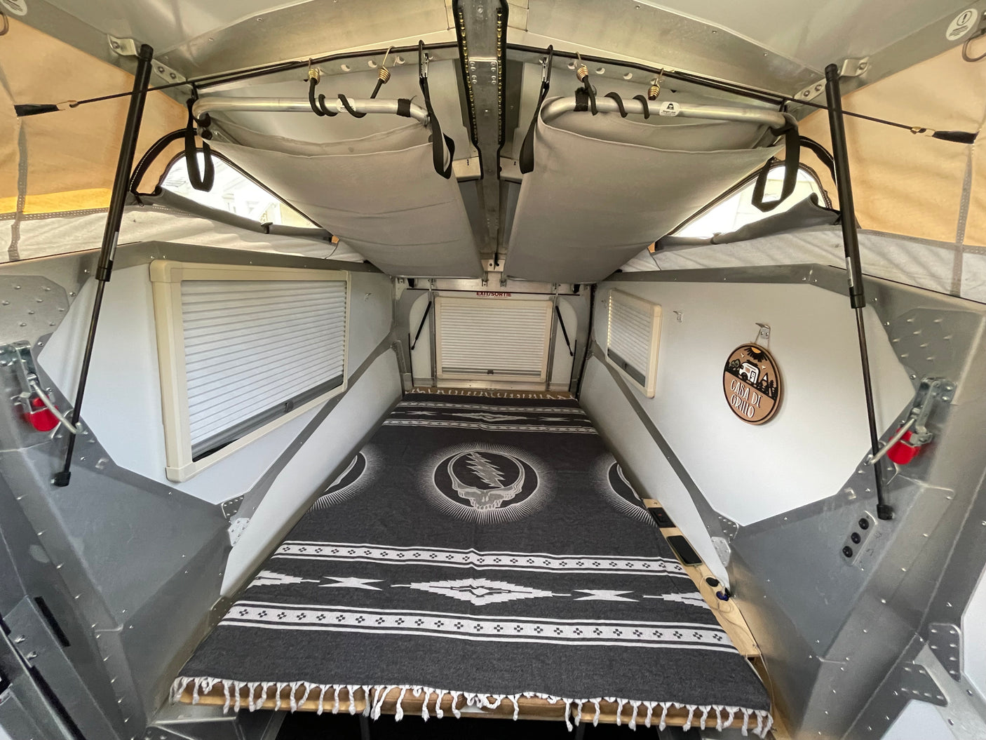 Cozy RV rental pop-up camper interior with a Grateful Dead blanket, blinds, and overhead storage.