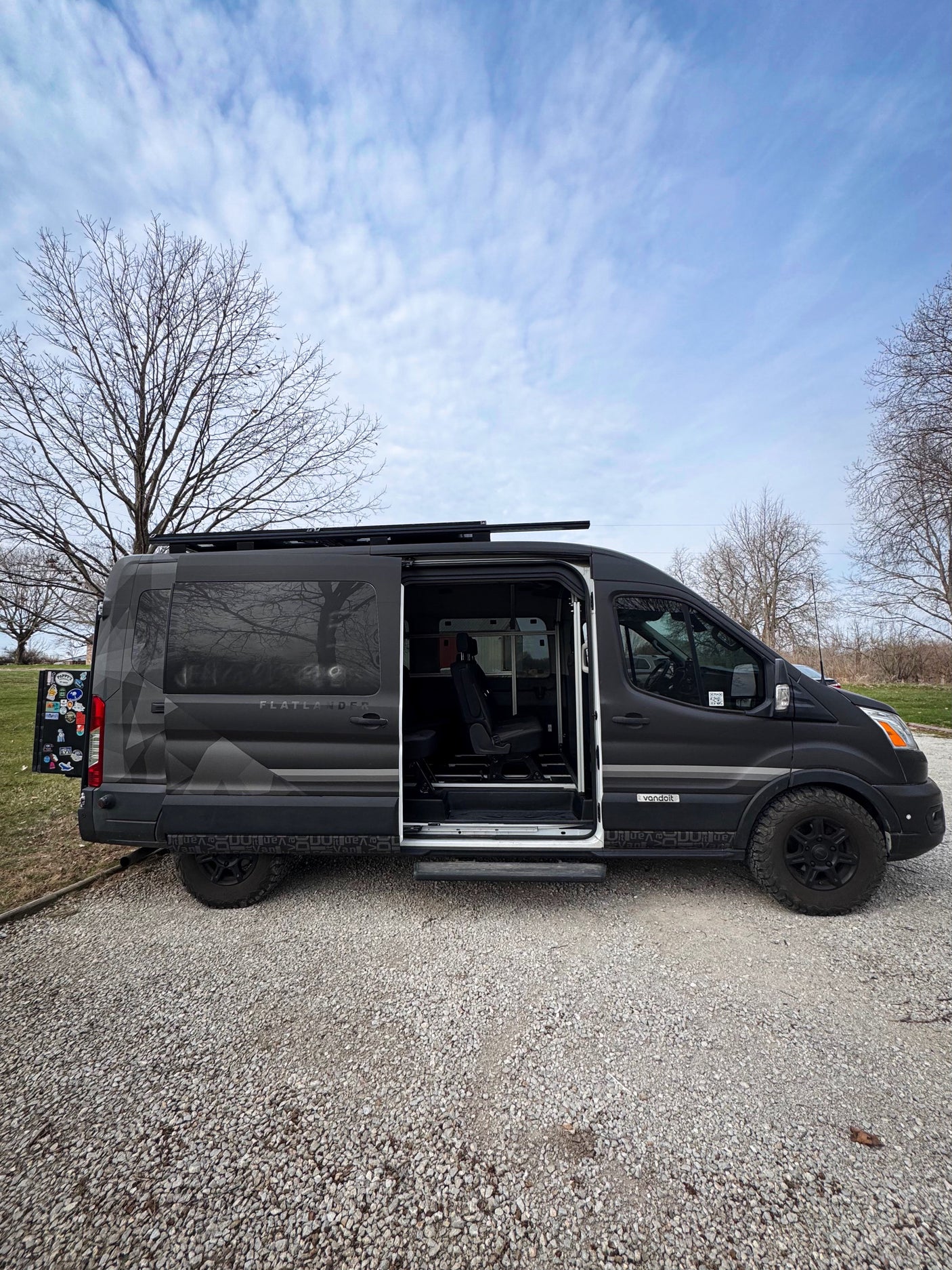 Explore with this dark grey Flatlander vandoit rv rental van on gravel, side door open. Perfect for van life adventures.
