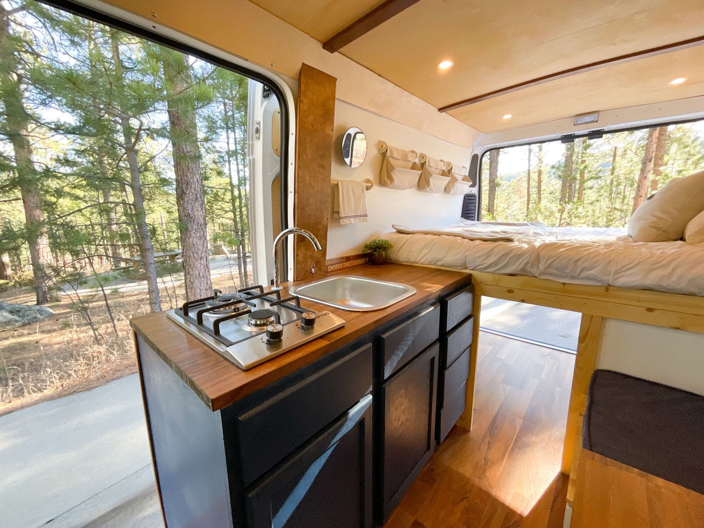 Bright rv rental camper van kitchen & bed with forest view. Features stove
