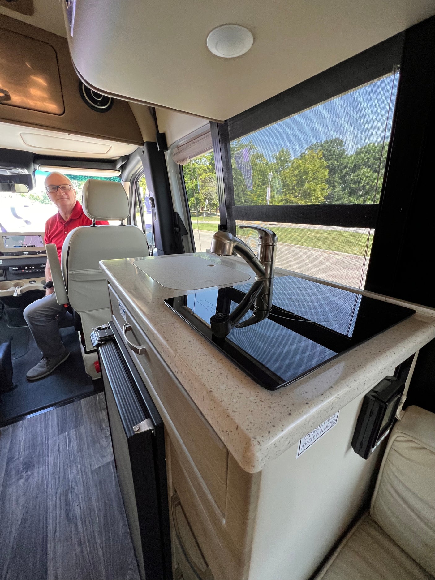 Step inside this RV rental: a bright interior showcasing a modern kitchen with a sink and cooktop, and a man in the driver's seat.