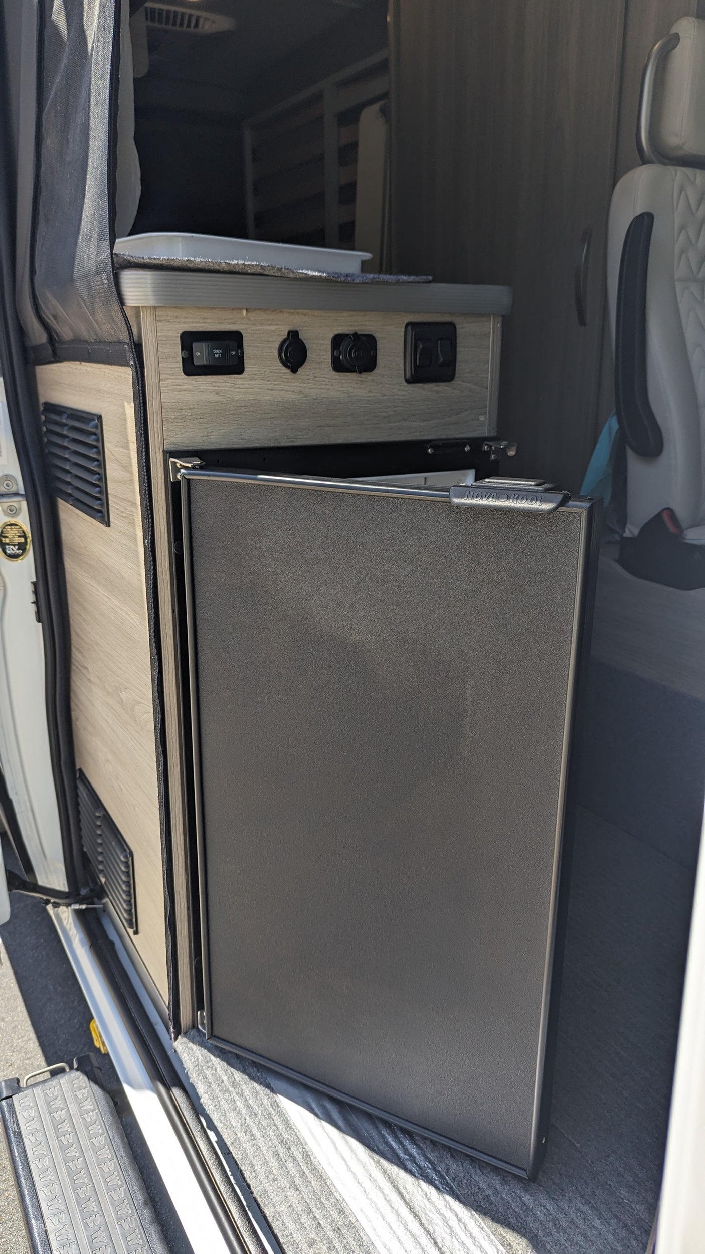 An RV rental's interior featuring a compact Nova Kool refrigerator, power outlets, and a control panel.