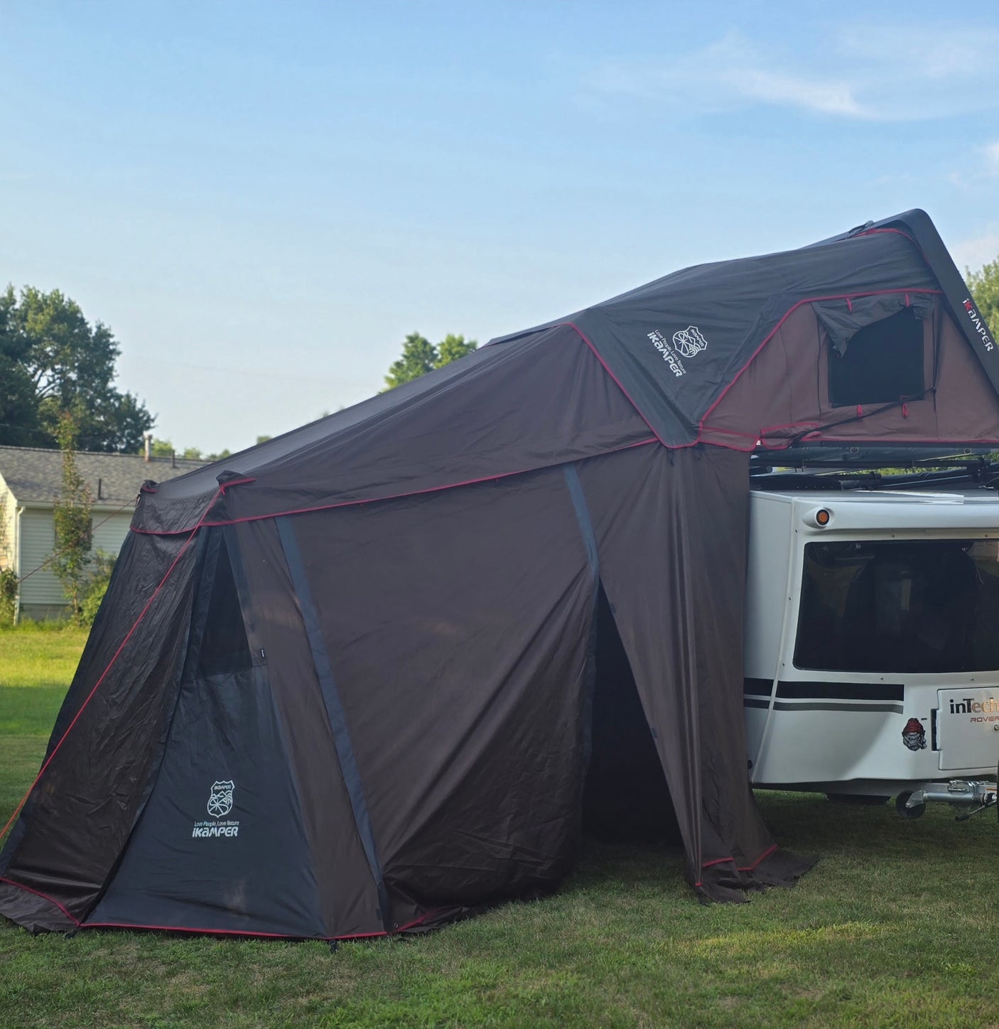 A dark brown iKamper rooftop tent and attached annex provide spacious camping next to a white trailer, ideal for RV rental trips.