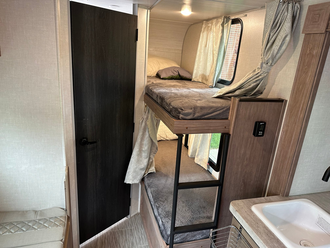 Compact RV rental interior with bunk beds, small sink, and a door. Perfect for maximizing space on the go.