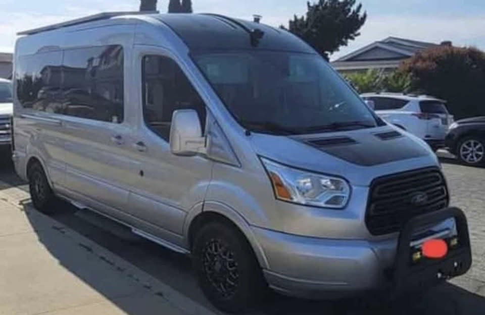 This silver Ford Transit camper van RV rental features a high roof, custom wheels, and a front bull bar.